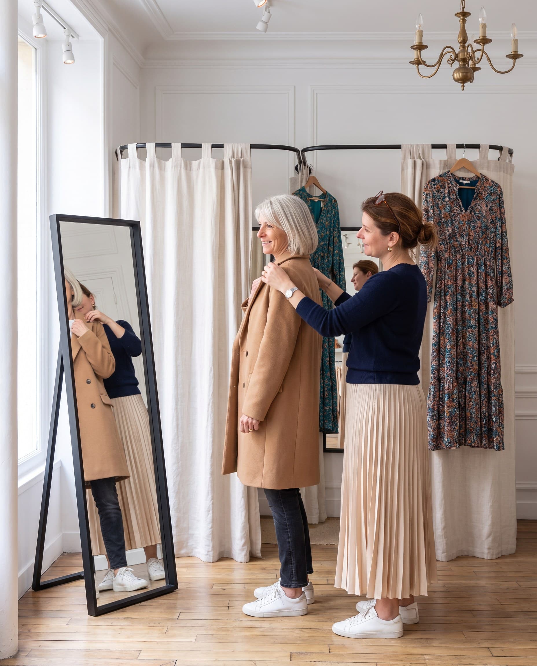 Claire ajuste un manteau camel sur une cliente devant le miroir