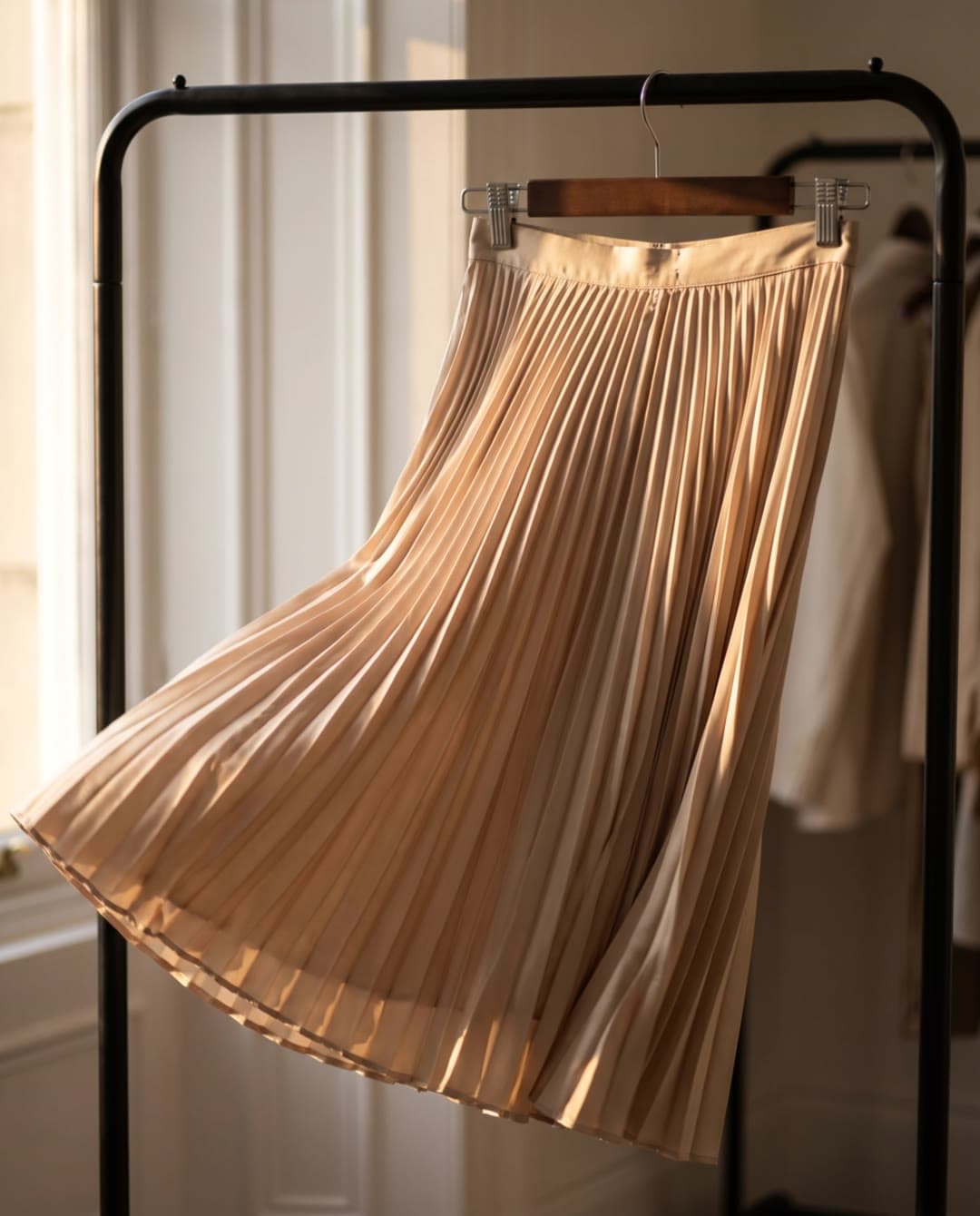 Une jupe plissée en satin champagne oscille doucement sur son portant